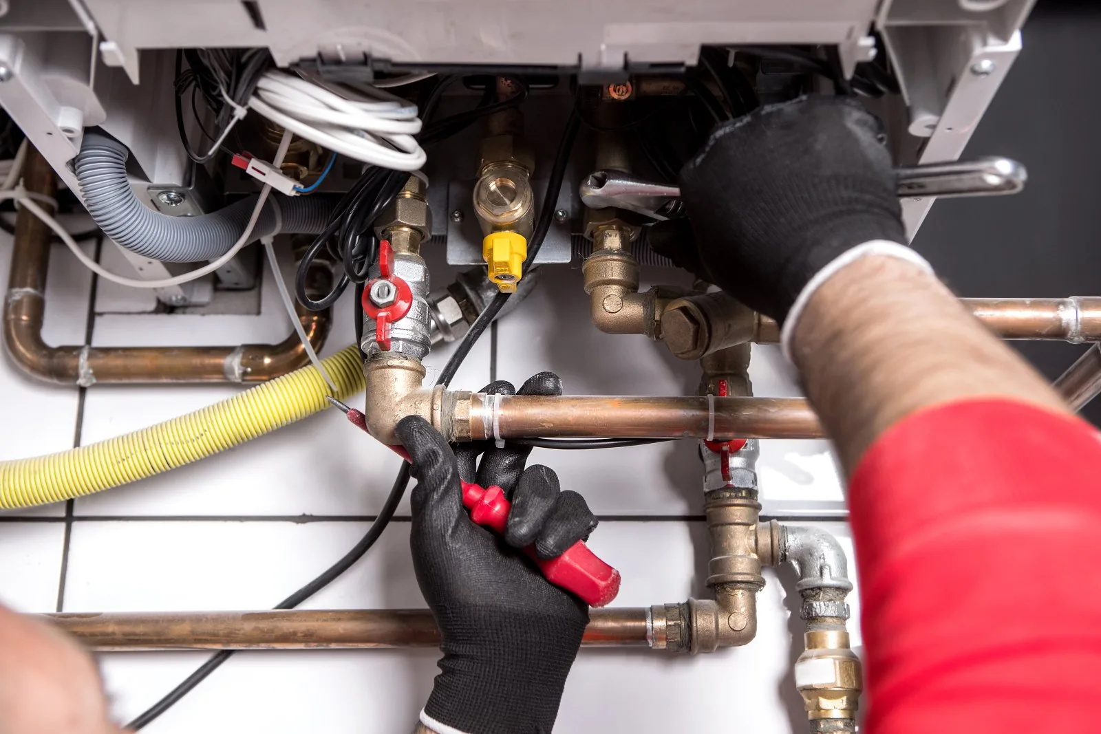 Technician installing brass valves and fittings on copper pipework below a boiler