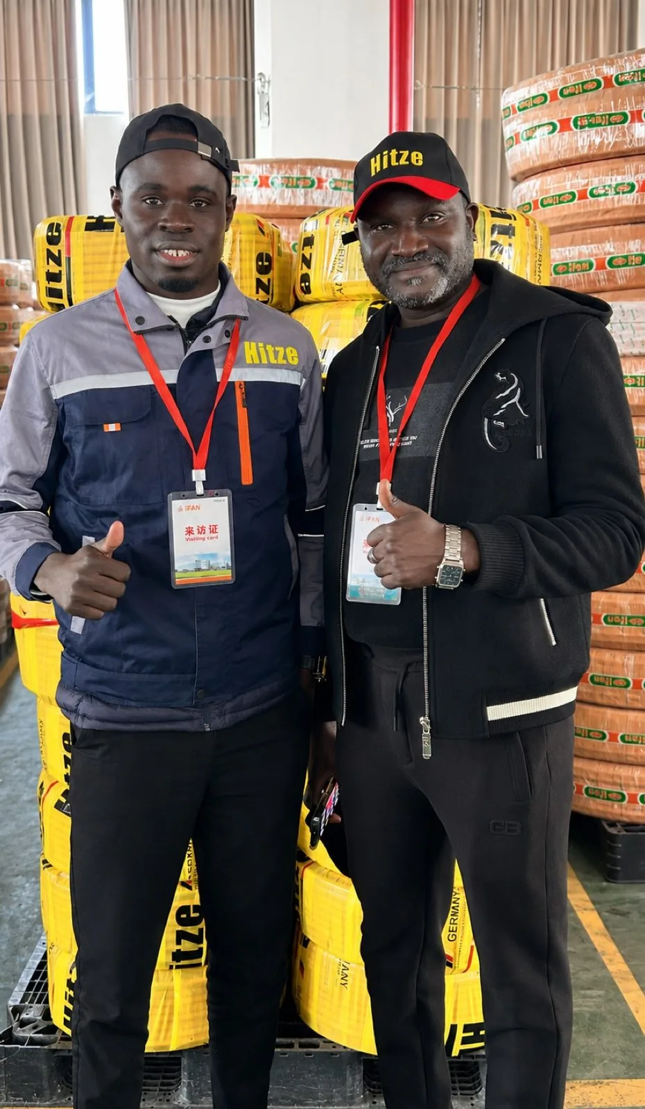 Two distributor partners giving a thumbs-up beside stacked Hitze pipe in the warehouse