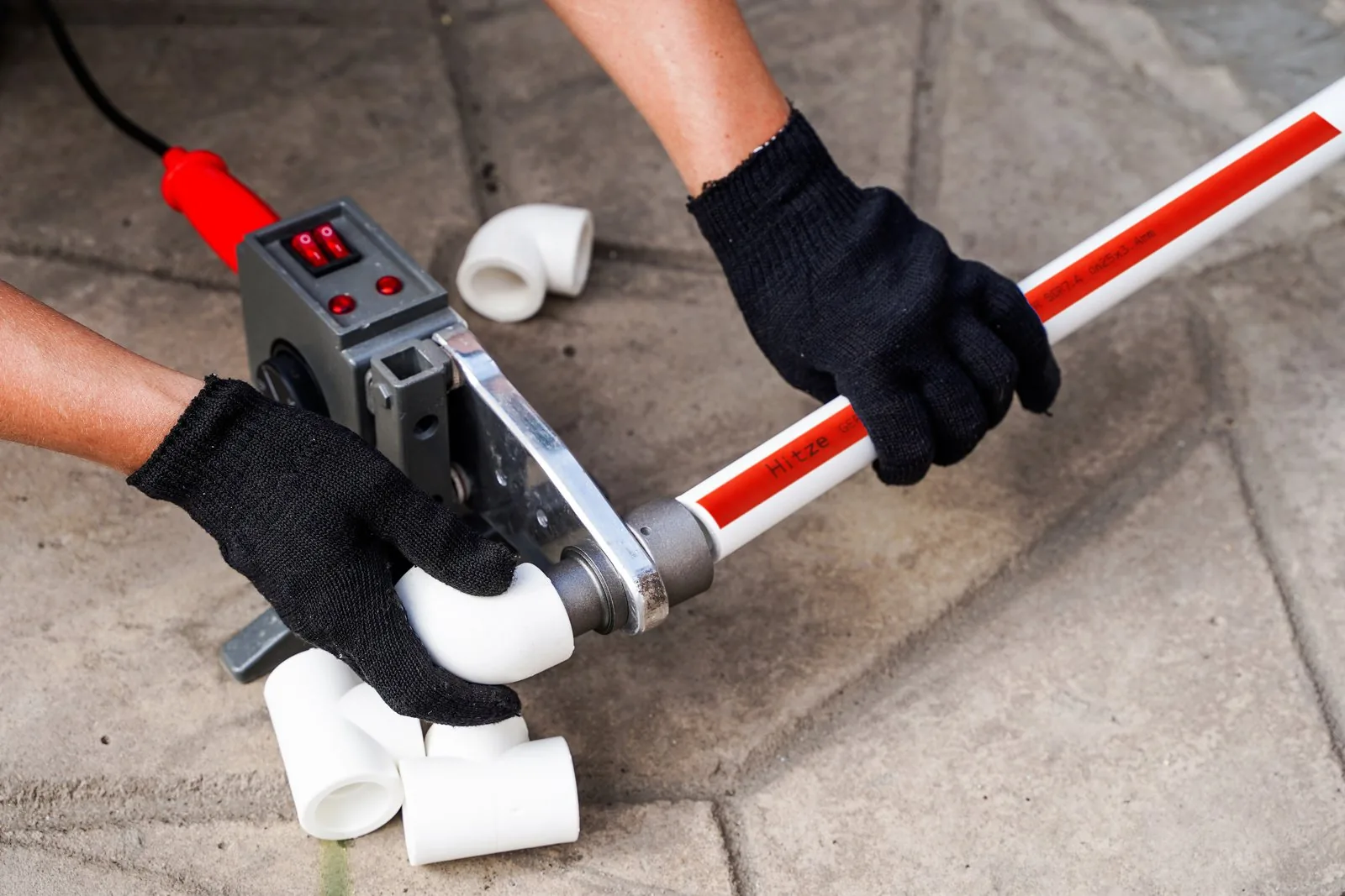 Socket-fusion tool clamping red-stripe PP-R pipe with white fittings ready to weld