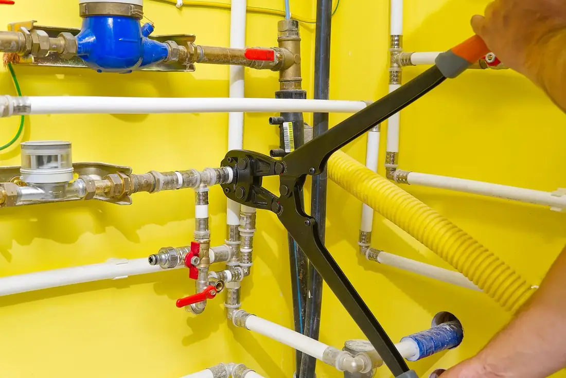 Press tool crimping a fitting on a wall of pipework in a plant room