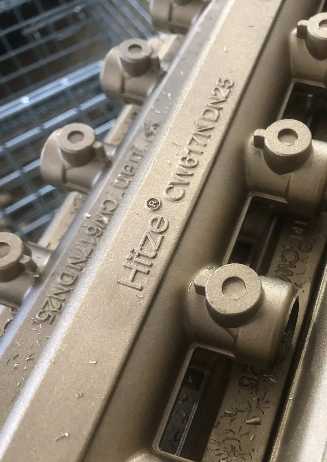 Macro of a cast manifold body showing the Hitze CW617N DN25 grade and size marking
