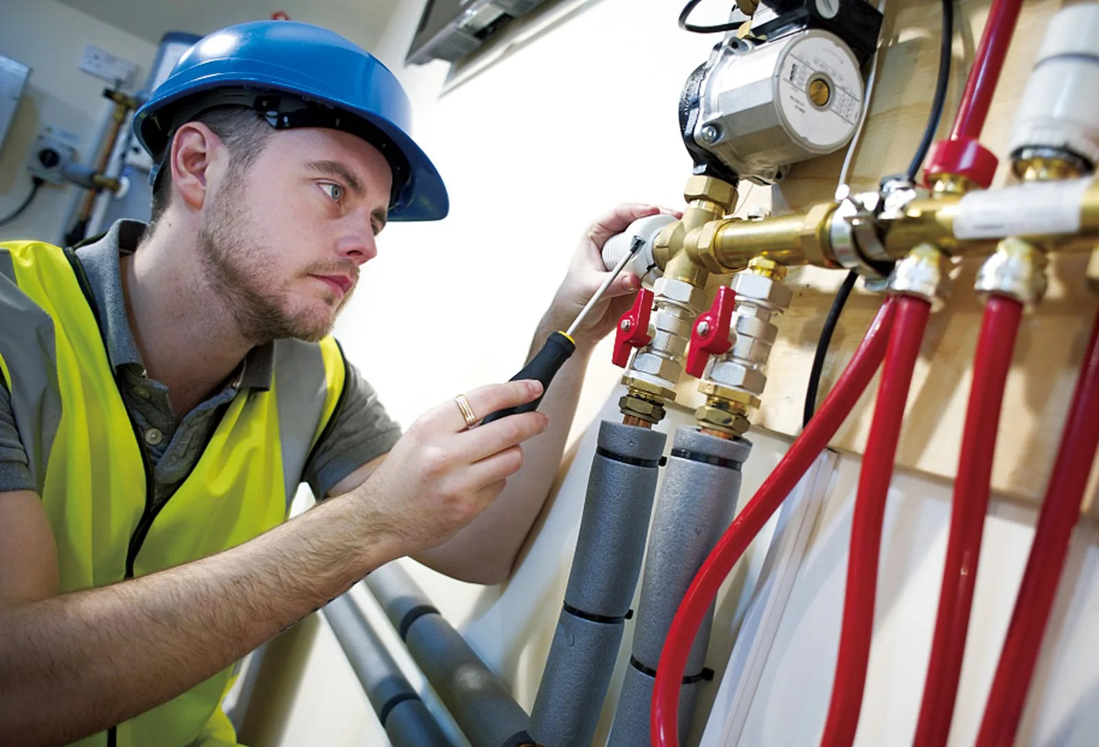 Installer connecting red heating pipe to a manifold with isolation valves and circulator pump during commissioning