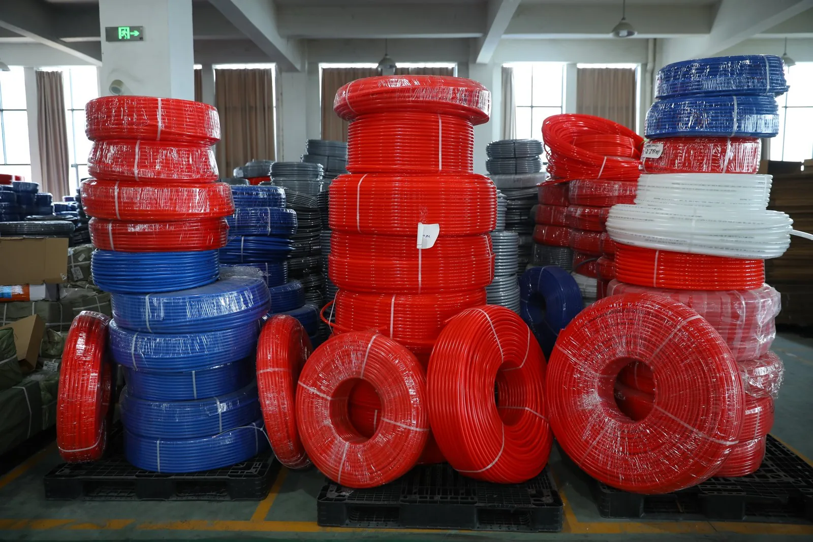 Stacked coils of red and blue oxygen-barrier underfloor heating pipe on pallets in a warehouse
