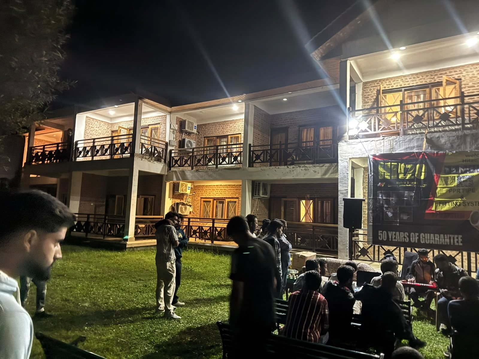 The Hitze Plumbers' Meet at night on the lawn, with the Hitze banner on the lodge