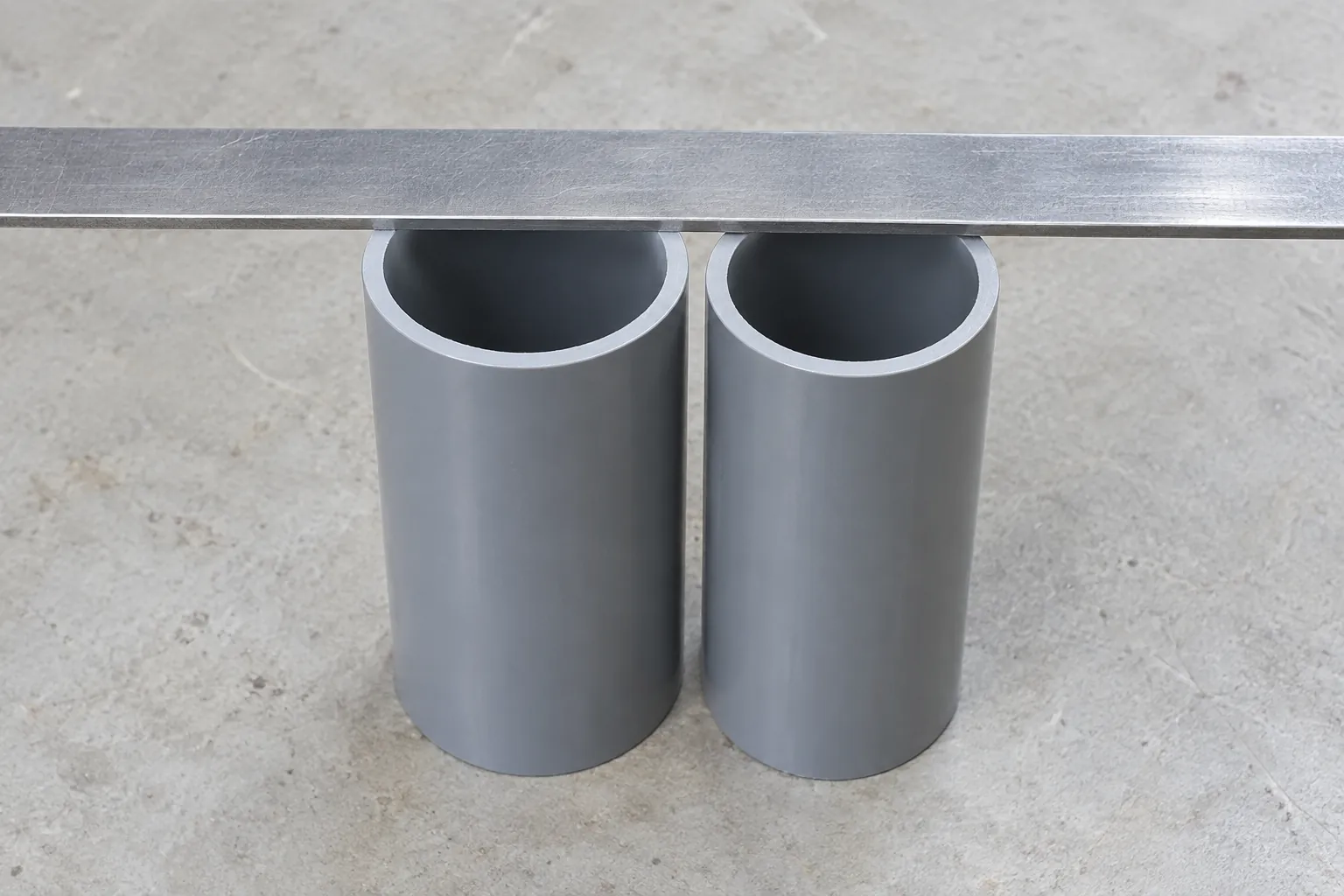 Two grey PVC pipe ends standing side by side under a steel straightedge laid across both tops